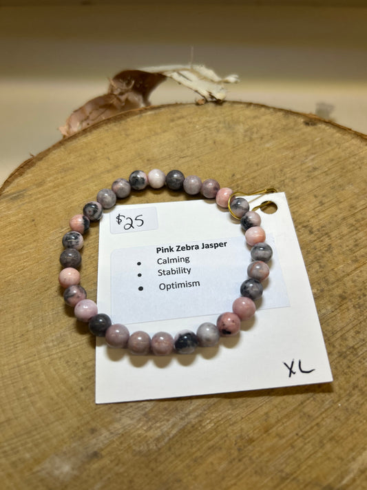 Pink Zebra Jasper bracelet on a wooden surface with a label detailing properties and price.